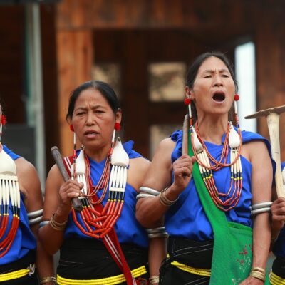A group of 4 women standing side by side in traditional dress and singing.